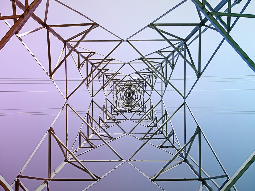 View looking up at the geometric metal structure of an electricity pylon, vital for mining energy, with power lines extending across a gradient sky. - Alwande Tech