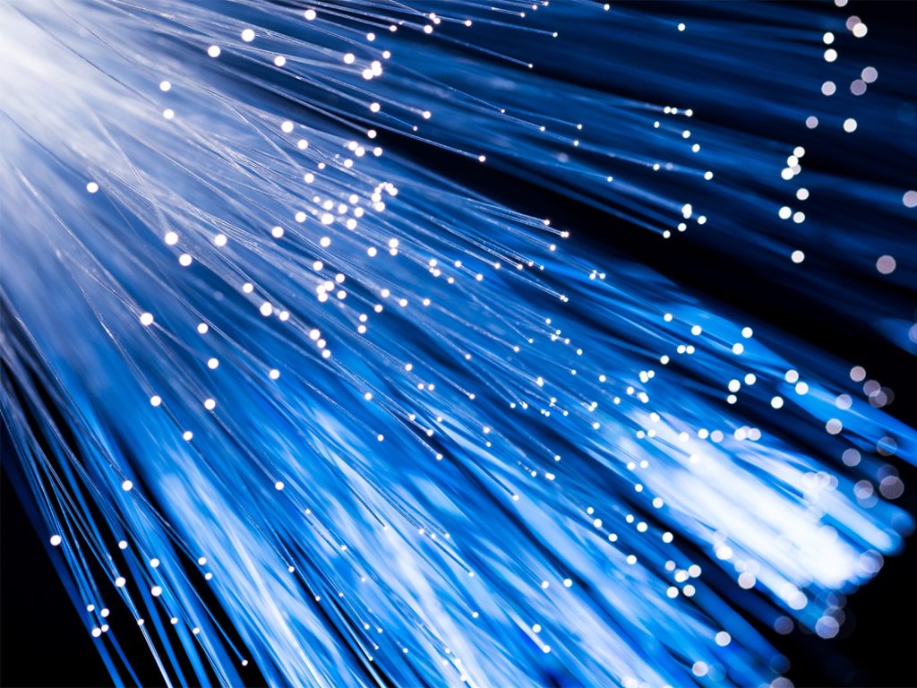 Close-up of blue fibre optic cables emitting light, with glowing dots representing data transmission against a dark background. - Alwande Tech