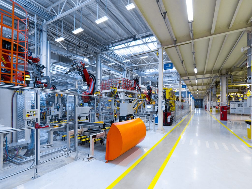 A modern factory interior with robotic arms, machinery, and bright lighting; yellow lines mark walkways on the clean polished floor. - Alwande Tech